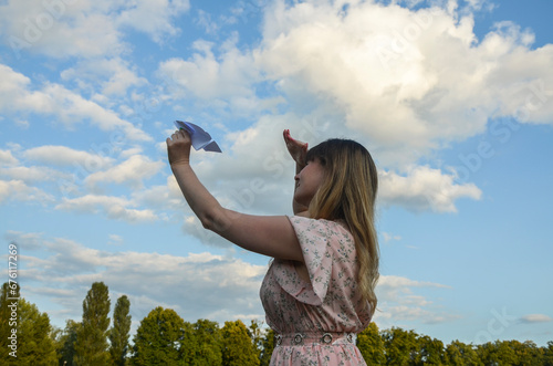 Attractive woman raising up paper plane toward sky. Dreaming of planning for the future travel