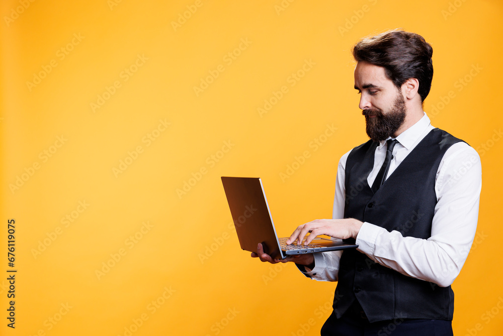 Young waiter browses webpage on laptop, searching for something on social media site on camera. Professional focused butler using pc with internet, working on restaraunt menu online. Young waiter browses webpage on laptop, searching for something on social media site on camera. Professional focused butler using pc with internet, working on restaraunt menu online.