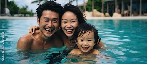 The Asian family spent a happy summer together by the pool with their cute child splashing in the blue water their smiles radiating pure joy in a portrait of happiness