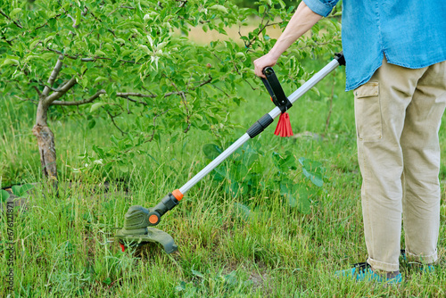 Woman mowing grass with cordless trimmer in garden