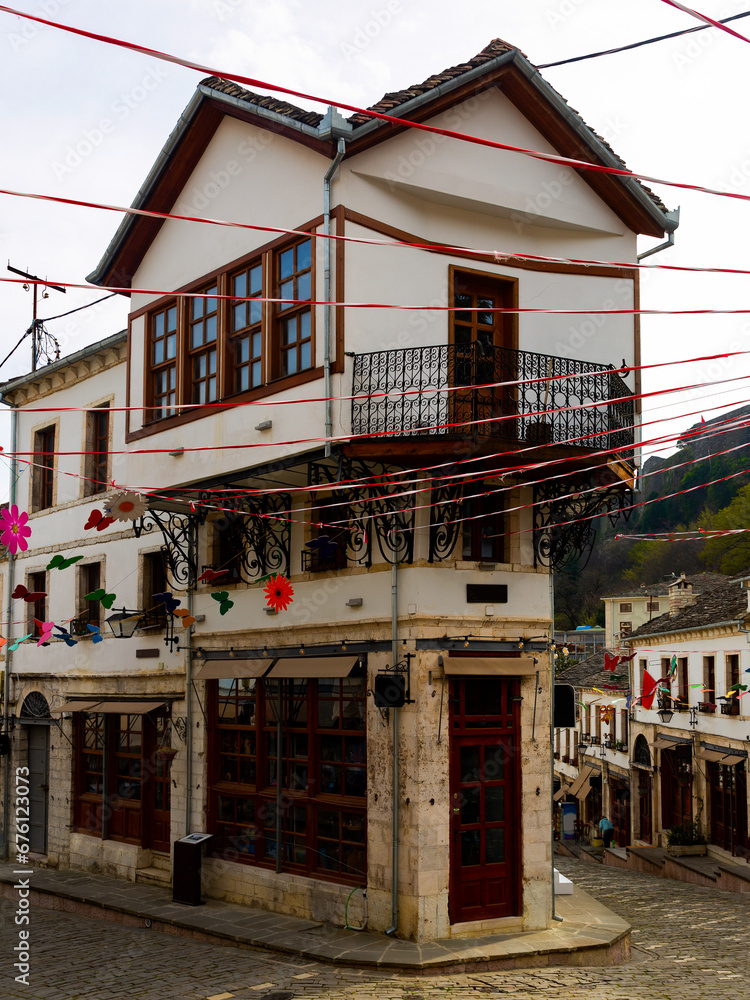 Scenic view of winding cobblestone streets in historic center of Gjirokaster decorated with colorful garlands for traditional spring festival of Dita e Veres and peculiar Ottoman era houses, Albania.
