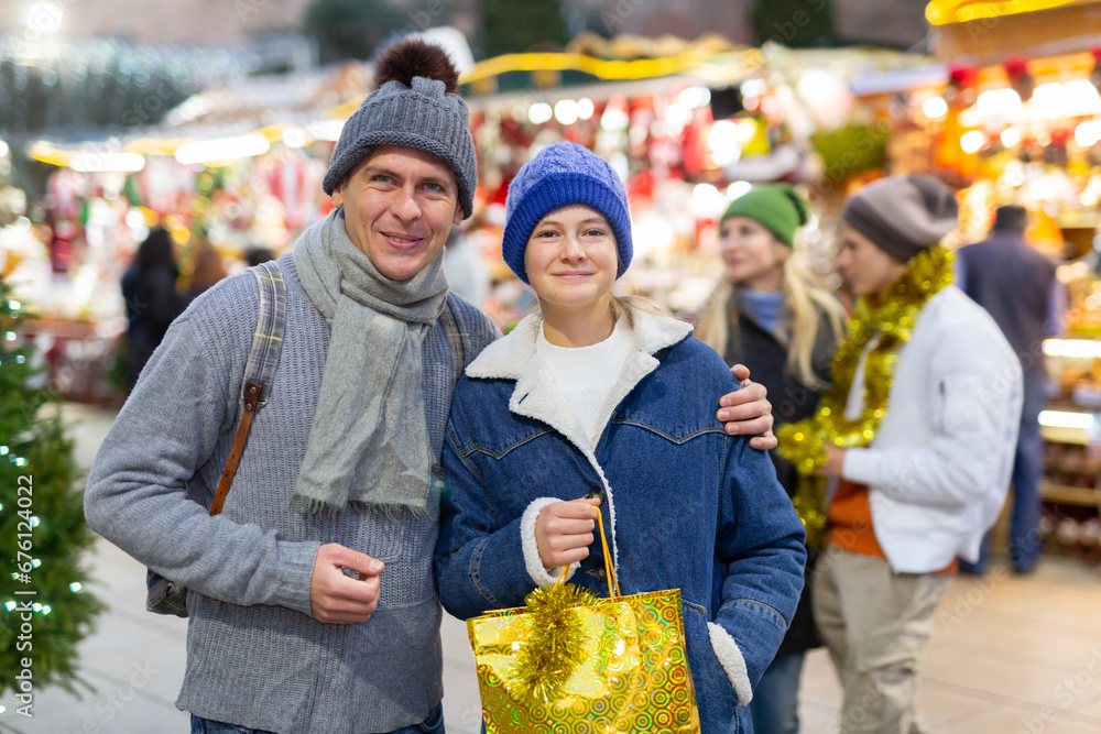 Smiling adult father with his teenager daughter posing with christmas gifts at Xmas market