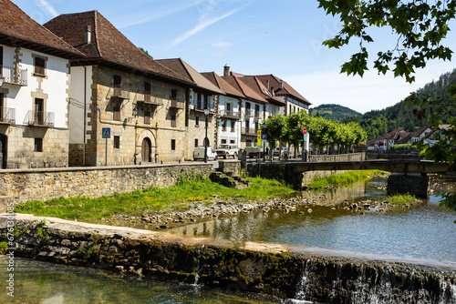 Ochagavia townscape on sunny summer day overlooking typical residential buildings with steep brown tiled roofs along stone embankment and bridge across Anduna river on sunny day, Navarra, Spain photo