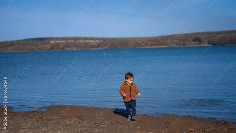 Baby boy having fun throwing stones into river. Kid cheerfully takes another stone and tossing into water. Baby boy having fun throwing stones into river. Kid cheerfully takes another stone and tossing into water.