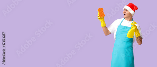 Male cleaner in Santa hat and with supplies on lilac background with space for text