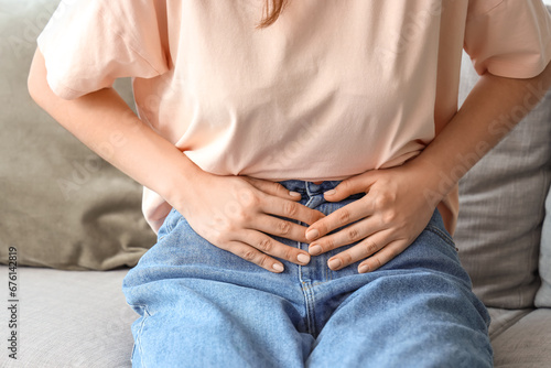 Young woman sitting on sofa and suffering from abdominal pain at home photo