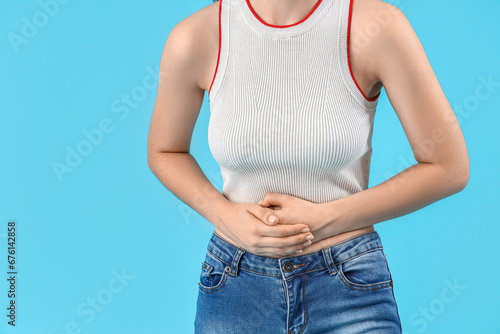 Young beautiful woman suffering from abdominal pain on blue background, closeup