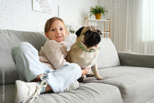 Little girl with cute pug dog sitting on sofa at home