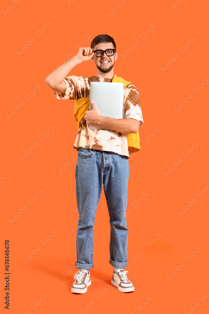 Young bearded man with laptop on orange background