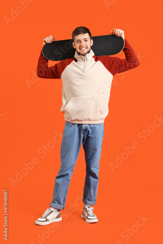 Young bearded man with skateboard on orange background