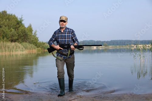 Man with hunting rifle near lake outdoors