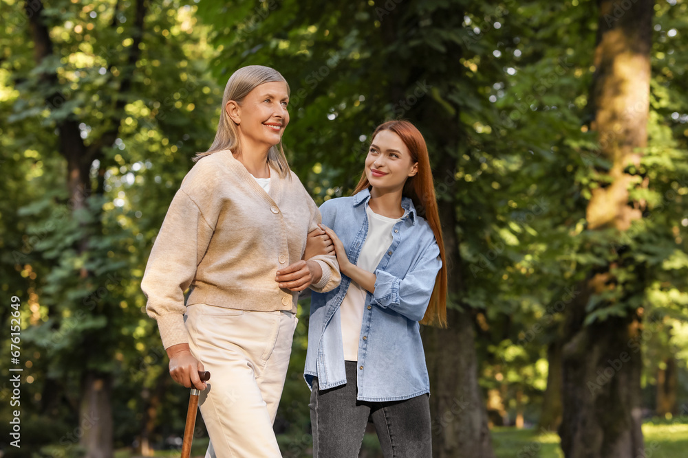 Senior lady with walking cane and young woman in park. Space for text