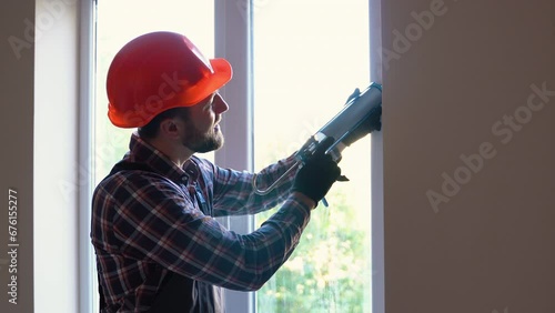 Handyman is applying polyurethane foam to fill gap between sash and window frame photo