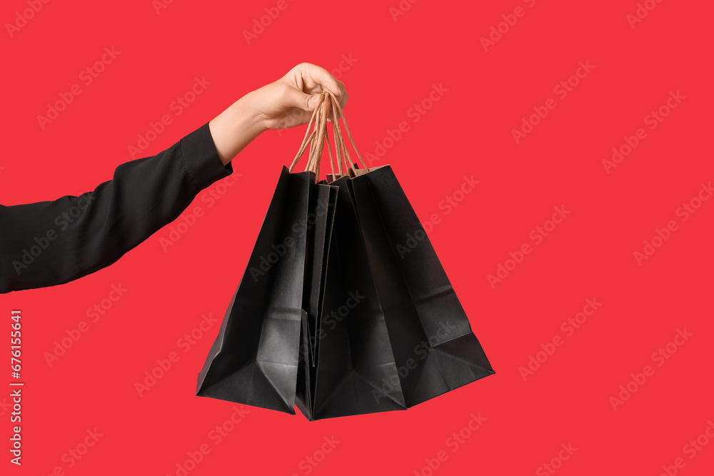 Female hand with shopping bags on red background. Black Friday Sale