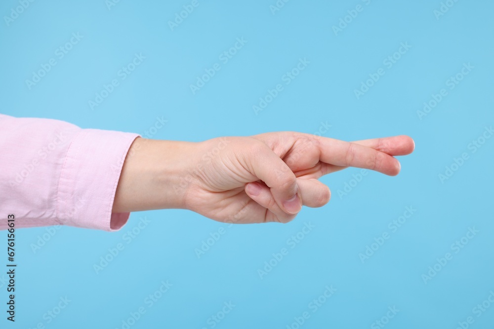 Woman crossing her fingers on light blue background, closeup