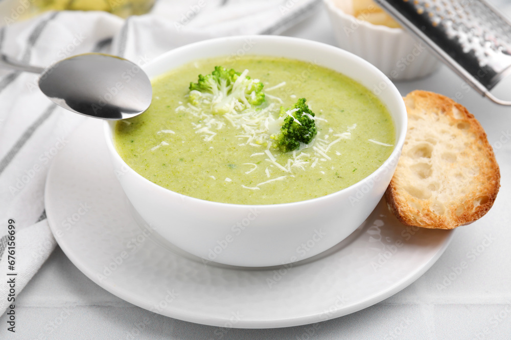 Delicious broccoli cream soup with cheese served on white tiled table, closeup