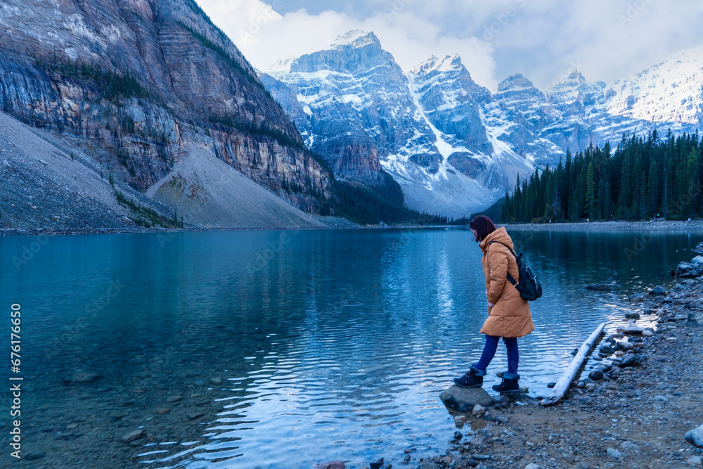 Female tourist carries a backpack, travels, walks, admires the beauty of the reflection in the water of moraine Lake, Canadian Rocky Mountains