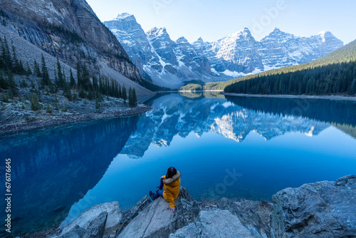 Female tourist carries a backpack, travels, walks, climbs, sits and admires the beauty of the reflection in the water of moraine Lake, Canadian Rocky Mountains photo