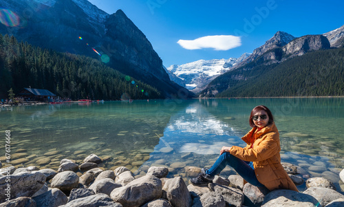 Asian female tourist backpacking, sitting, admiring the beauty of Lake Louise Banff, Canadian Rocky Mountains National Park