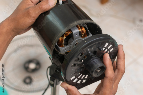 A technician removes the front casing to reveal and inspect the motor of an oscillating electric fan. Cleaning and repairing an electric stand fan.