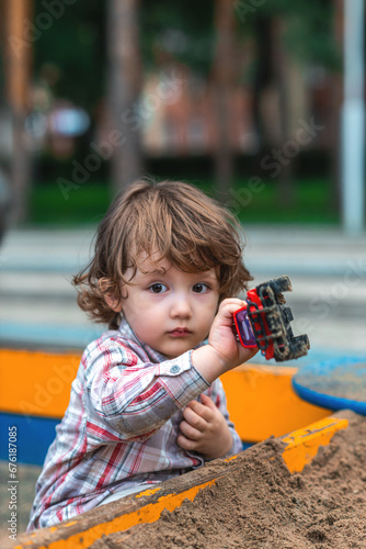 little boy playing in the sandbox with a car