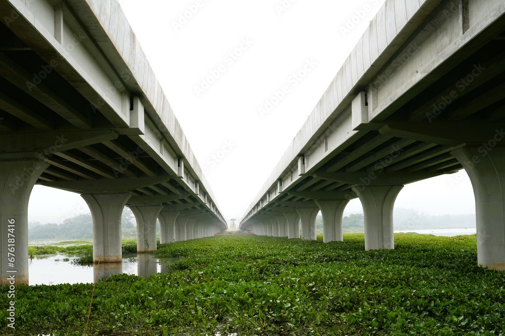 Photo taken from below two large bridges crossing the river in beautiful parallel lines on a slightly misty morning.