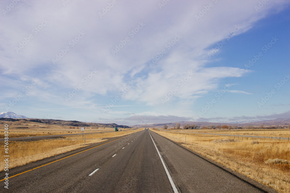 Beautiful landscape with a road among yellow dry grass and snow-covered mountains on the horizon.