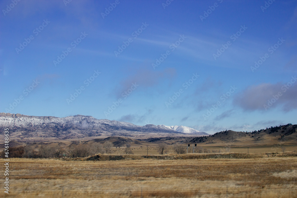 Beautiful landscape with a road among yellow dry grass and snow-covered mountains on the horizon.