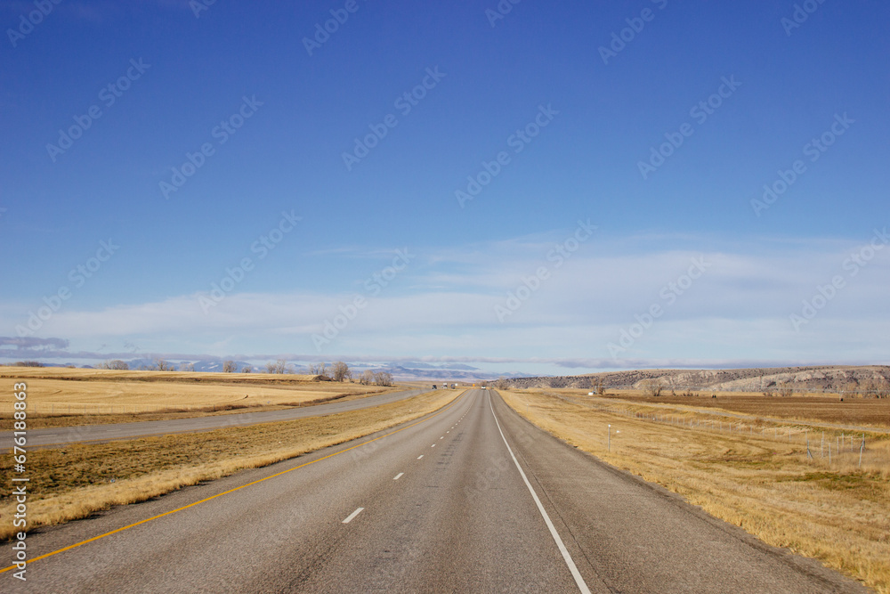 Beautiful landscape with a road among yellow dry grass and snow-covered mountains on the horizon.