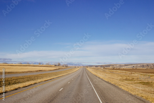 Beautiful landscape with a road among yellow dry grass and snow-covered mountains on the horizon.