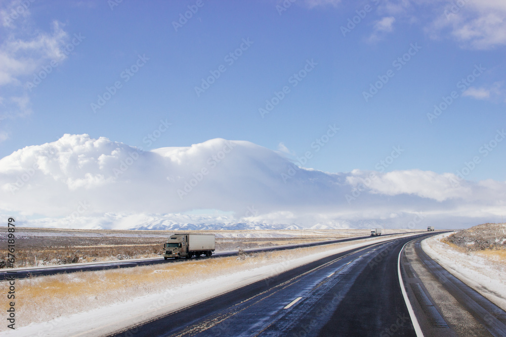 Steep highway among snow-capped mountains on a sunny winter day. Bright blue winter sky with large clouds over an asphalt road. Highways in USA. American roads Steep highway among snow-capped mountains on a sunny winter day. Bright blue winter sky with large clouds over an asphalt road. Highways in USA. American roads