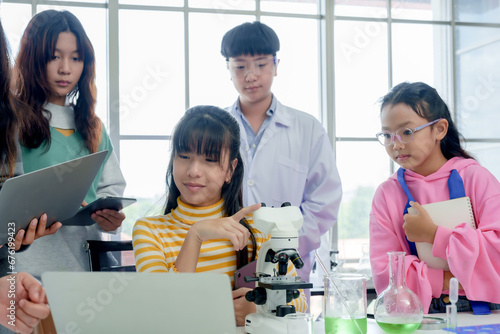 Asian school girl Carrying tablet and notebook he researched experiments from the internet that the science teacher was teaching. A boy using microscope to look at cell samples in the science room. photo