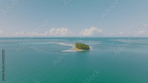 Aerial shot - Discover of tiny island with forest and no people in the middle of the ocean. Palm trees in the charming paradise with white sand. Blue ocean lagoon in sunny day. photo