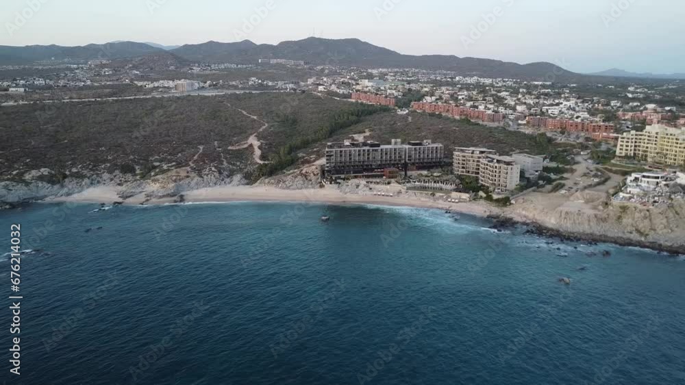 Aerial view over the coastline from monument beach at the cape thompson hotel in los cabos overlooking the boardwalk, blue sea with calm waves and the hotel grounds during a vacation in mexico Aerial view over the coastline from monument beach at the cape thompson hotel in los cabos overlooking the boardwalk, blue sea with calm waves and the hotel grounds during a vacation in mexico