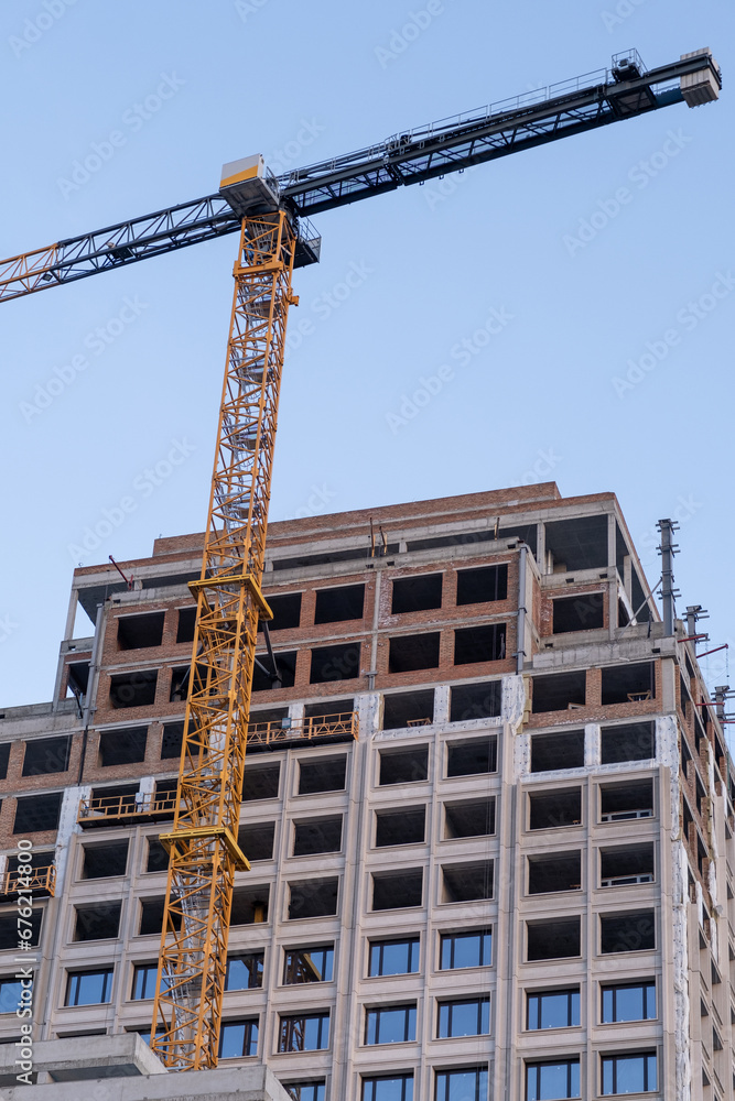 A crane and a building under construction against a blue sky background. Builders work on large construction sites, and there are many cranes working in the field of new construction.