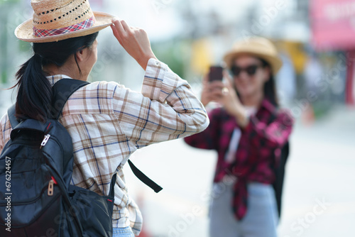 Two young Asian female tourists shopping, holding shopping bags and walking happily, enjoying shopping together and taking selfies with smartphones. Taking pictures. Vacation concept, lifestyle.