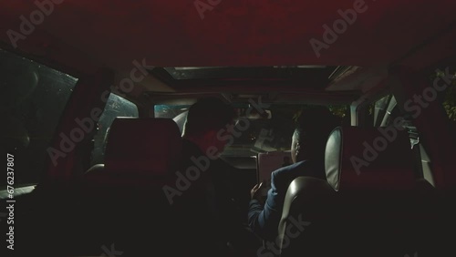 Rear view shot of two police operatives sitting in car at night, examining criminal profile folder and having discussionRear view shot of two police operatives sitting in car at night, examining crimi photo