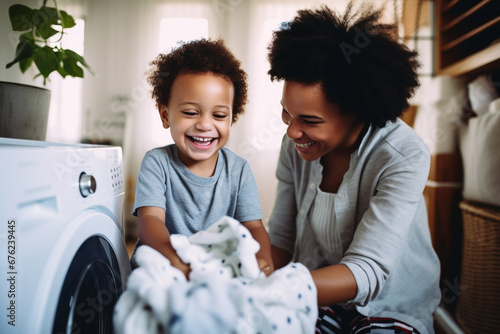 Adorable little African American boy with an afro smiling and faving fun while doing housework with him mother at home, mixed race shot of a cute child folding laundry with his mom
