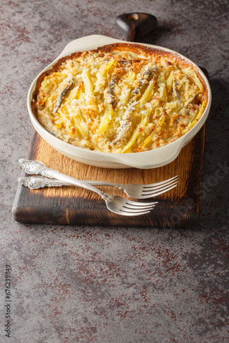 Janssons frestelse casserole consists of potatoes and anchovies which are layered with onions and then doused in cream closeup on the baking dish on the table. Vertical