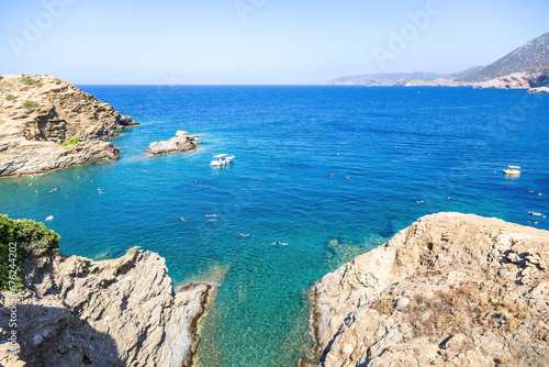Greece island. Moored boat in Aegean sea, sunny day. People swim in turquoise water background.