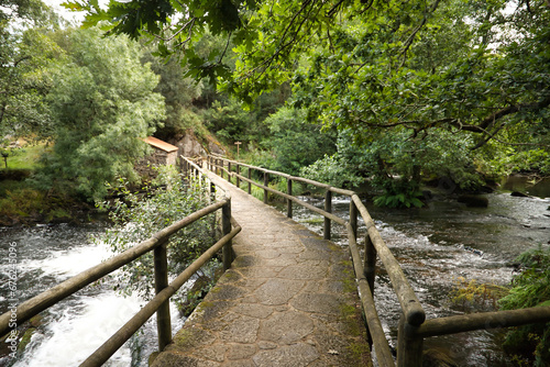 Stone bridge over a beautiful landscape formed by small waterfalls on stones within a lush and green forest. Concept landscape, water, forest, vegetation, humidity. © Manuel