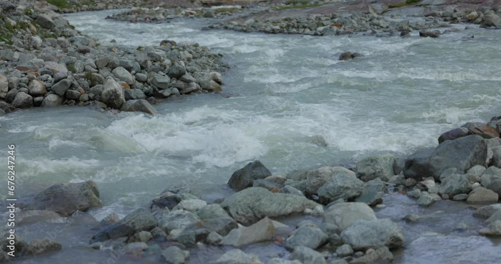 Flowing River Past Small Rock Boulders Near Fellaria Glacier. Slow Motion, Pan Up Shot Flowing River Past Small Rock Boulders Near Fellaria Glacier. Slow Motion, Pan Up Shot