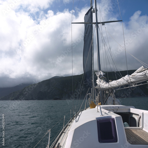 Approaching uninhabited wild rocky coast with mountains on sail yacht, Staysail laid on boom, reaching the goal concept, traveling Kamchatka  photo