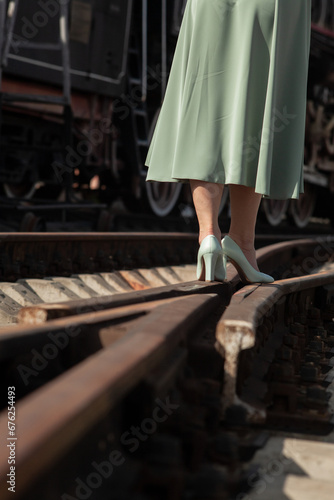 A girl in a green dress and heels, standing at the intersection of the trains on the background of a large locomotive