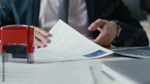 Close up cropped shot of unrecognizable executive manager stamping rejected on document and looking through other paperwork with European Union logo during work in office photo
