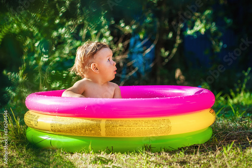 Photos A cute little baby boy is playing with toys while bathing in a little colorful wading pool on meadow garden field outdoor