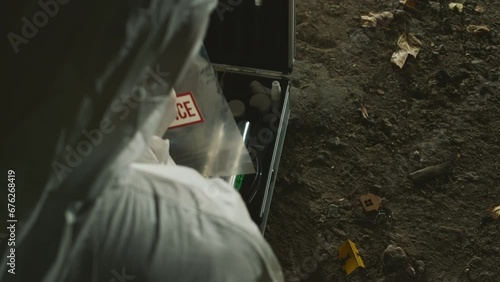 From above shot of anonymous forensic specialist in protective coveralls collecting evidence from ground in plastic bag and putting it into kit at murder scene at night photo