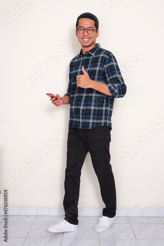 Full body portrait of a man smiling and give thumb up while holding mobile phone photo