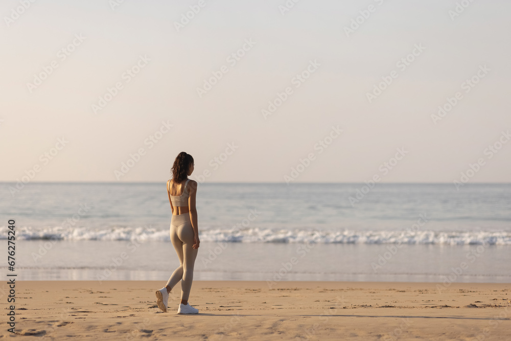 Back view of sportswoman runner standing resting after morning workout on sandy beach looking at the sea. High quality photo