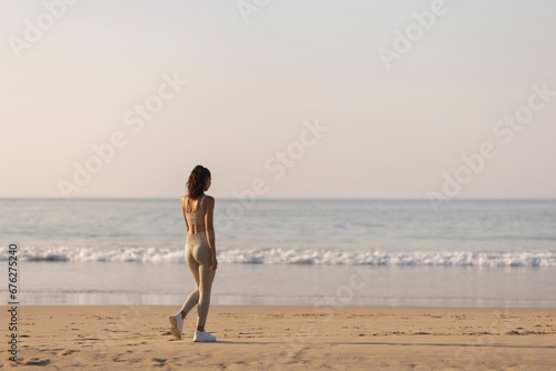 Back view of sportswoman runner standing resting after morning workout on sandy beach looking at the sea. High quality photo